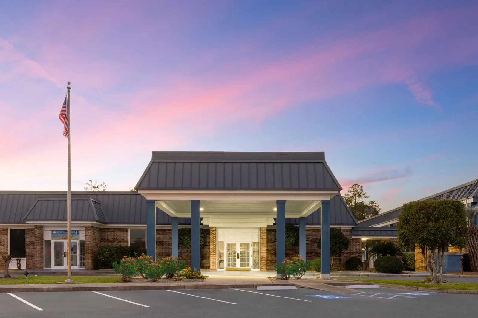 Days Inn Hinesville entrance at dusk with a flagpole and a lit covered canopy